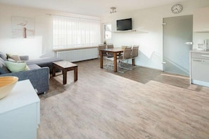 A modern living room with a sofa, coffee table, and dining table with chairs. - Holiday apartment in Juist with swimming pool (Juist)