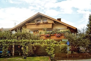A two-story wooden house with a balcony, surrounded by a garden with grapevines. - Holiday apartment with 2 bedrooms (Bernau a. Chiemsee)