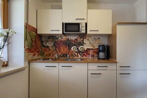 Eine Küche mit weißen Schränken, einer Mikrowelle, einer Kaffeemaschine und einer blumengemusterten Spritzschutzwand.