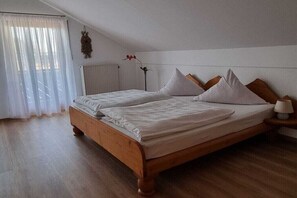 A bedroom with a wooden bed, white bedding, a bedside table with a lamp, and a window with sheer curtains. - Holiday apartment with 2 bedrooms (Bernau a. Chiemsee)