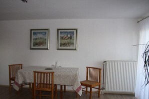 Ein Essbereich mit einem Tisch für vier Personen, zwei gerahmte Bilder an der Wand und einer Heizung.