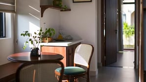 A kitchen area with a wooden table, a wicker chair, a potted plant, and a framed botanical illustration on the wall. - La Maison Gao (Hoi An Dong ward)