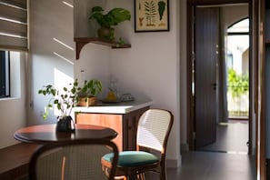 A kitchen area with a wooden table, a wicker chair, a potted plant, and a framed botanical illustration on the wall. - La Maison Gao (Hoi An Dong ward)