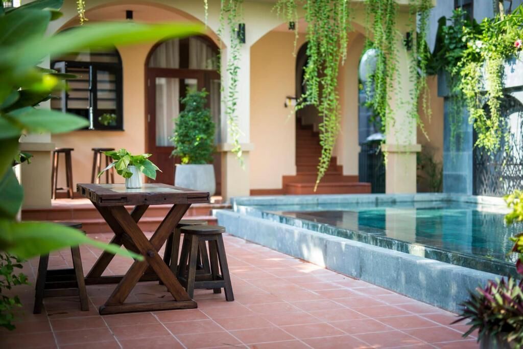 A pool area with a table and chairs, surrounded by arches and greenery.
