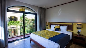A hotel room with a large bed, a nightstand, a lamp, and a view of a balcony with plants. - La Maison Gao (Hoi An Dong ward)