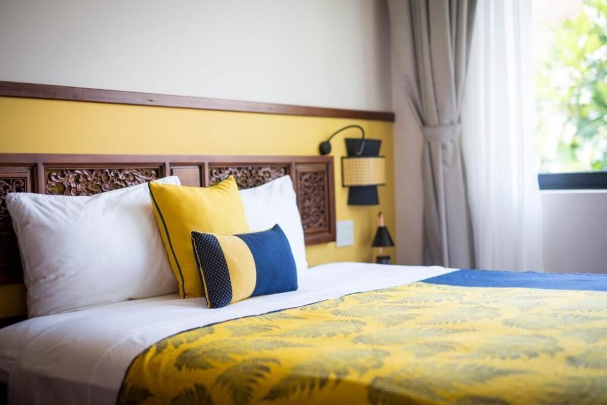 A hotel room with a bed, a headboard, a lamp, and a window with curtains.