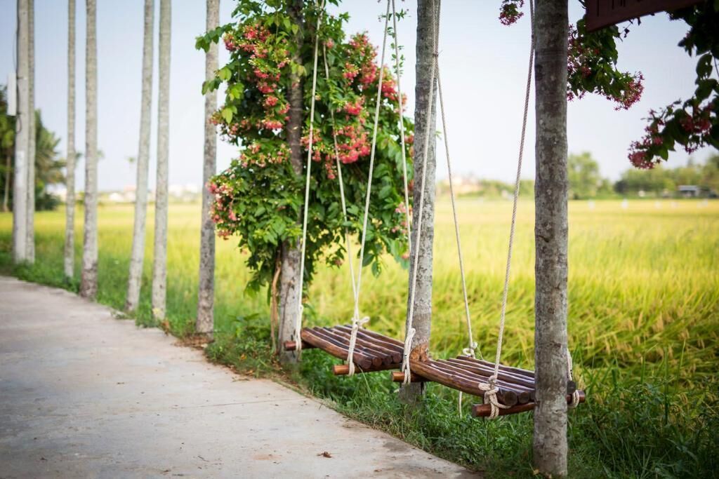 Una hamaca de madera colgada con cuerdas entre árboles en un campo cubierto de hierba.