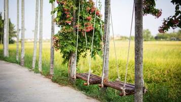 Una hamaca de madera colgada con cuerdas entre árboles en un campo cubierto de hierba.