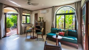 A room with a sofa, chairs, a small table, and a large window with a view of greenery. - La Maison Gao (Hoi An Dong ward)