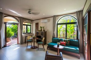 A room with a sofa, chairs, a small table, and a large window with a view of greenery. - La Maison Gao (Hoi An Dong ward)