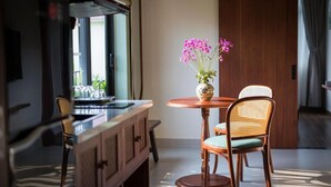 Un comedor con una mesa redonda, dos sillas de mimbre, un jarrón con flores y vistas al exterior a través de una ventana.