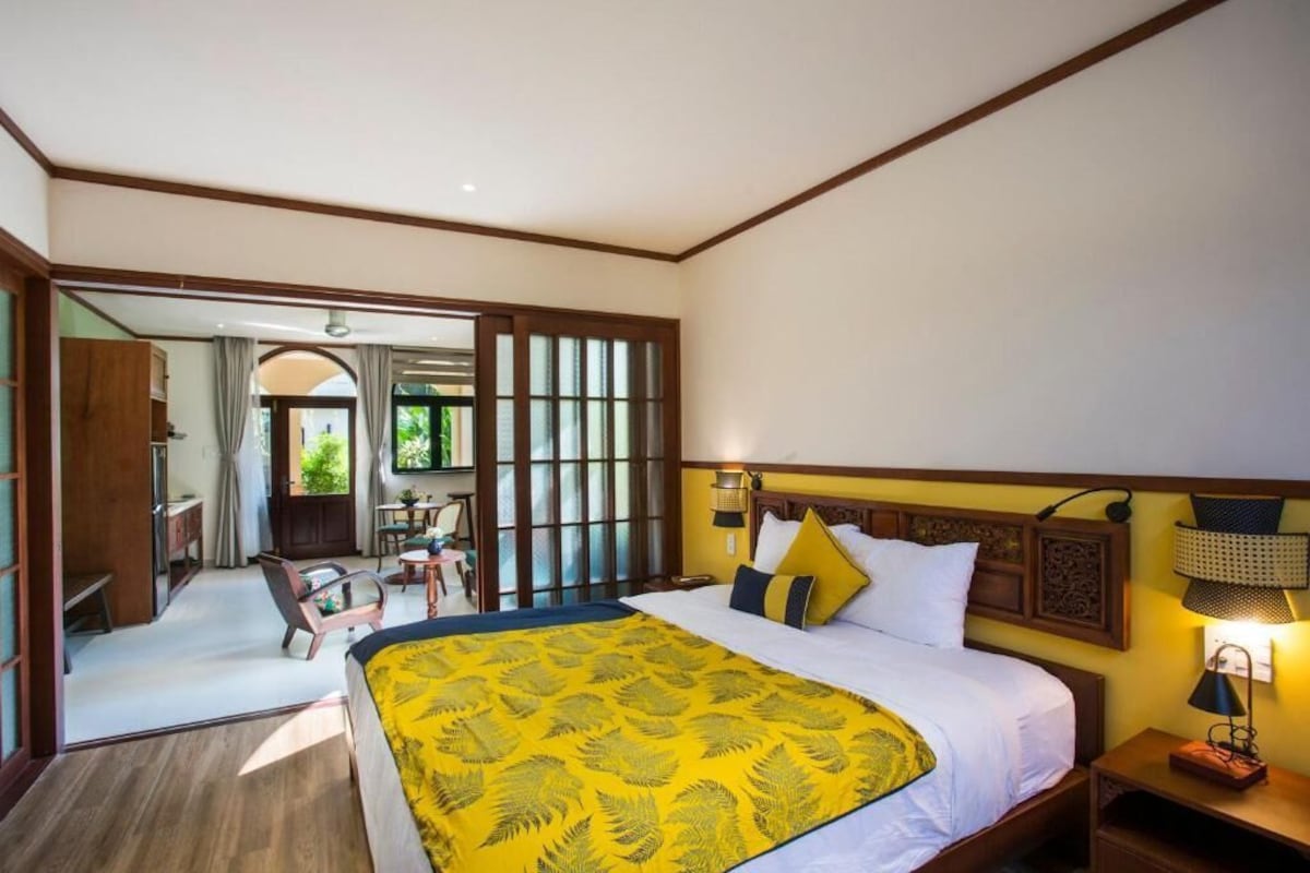 A hotel room with a bed, bedside lamps, a wooden headboard, and a view of the outdoor area.