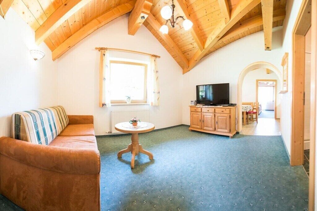 A cozy living room with a sofa, a small round table, a television, and wooden cabinets.