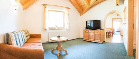 A cozy living room with a sofa, a small round table, a television, and wooden cabinets.