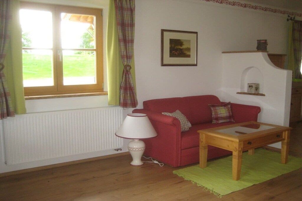 A red sofa, a wooden coffee table, a white lamp, and a window with curtains.