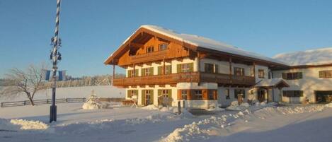 A two-story chalet with a balcony, surrounded by snow.