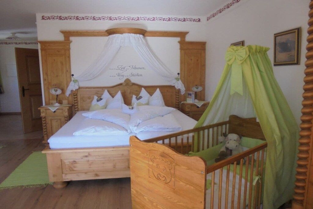 A bedroom with a wooden bed, a canopy, a crib, and a nightstand with a lamp.