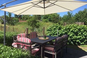 An outdoor patio with a table and chairs, a large umbrella, and a garden setting.
