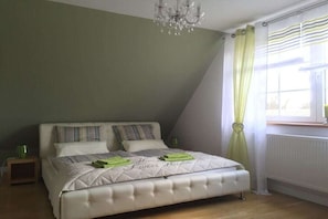 A bedroom with a bed, a nightstand, a chandelier, and a window with curtains.