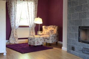 A living room with a fireplace, a floral armchair, a small table, and a purple rug. - Holiday home with 2 bedrooms (Letschin OT Gross Neuendorf)