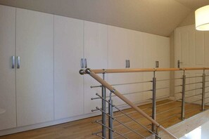 A staircase with a wooden handrail and metal balusters, leading to a room with white cabinets and a wooden floor.