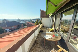 Un balcón con vistas a una zona residencial, una mesa redonda de madera y una ventana.