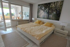 Un dormitorio con cama, mesita de noche, ventana con cortinas, radiador y un cuadro en la pared.