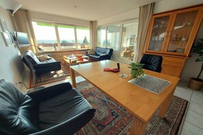 Ein modernes Wohnzimmer mit einem Holzespeisetisch, Ledersofas, einer Vitrine und großen Fenstern mit Blick.