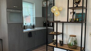 Eine moderne Küche mit grauen Schränken, einem eingebauten Ofen und einem Fenster mit Jalousien.