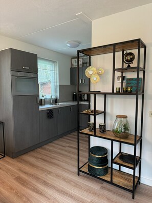 Een moderne keuken met grijze kastjes, een inbouwoven en een raam met zonwering.