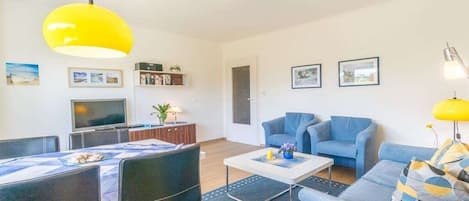 Uma sala de estar moderna com um sofá, poltronas, uma mesa de centro e uma televisão.