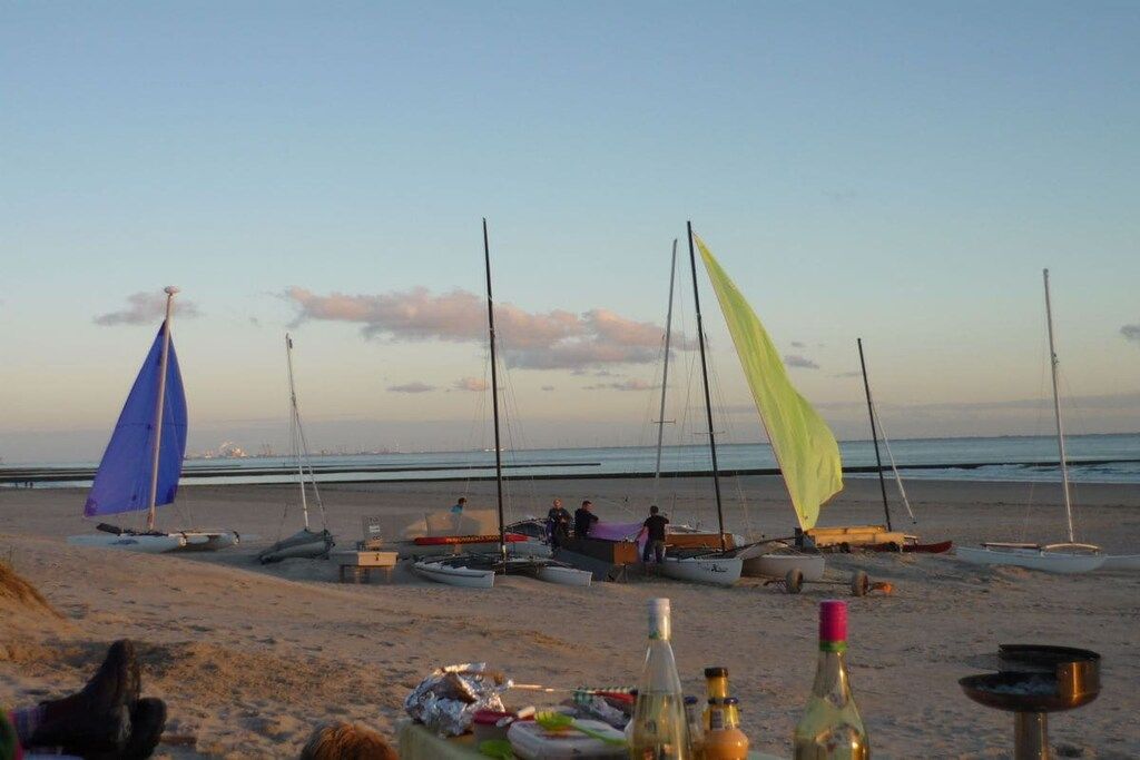 Ein Strand mit mehreren Segelbooten und einem Tisch mit Flaschen und Speisen.