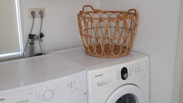 Un área de lavandería con lavadora y secadora, una cesta de mimbre y estantes de madera.