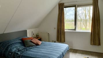 Un dormitorio con cama, un radiador, una ventana con cortinas y vistas a árboles.