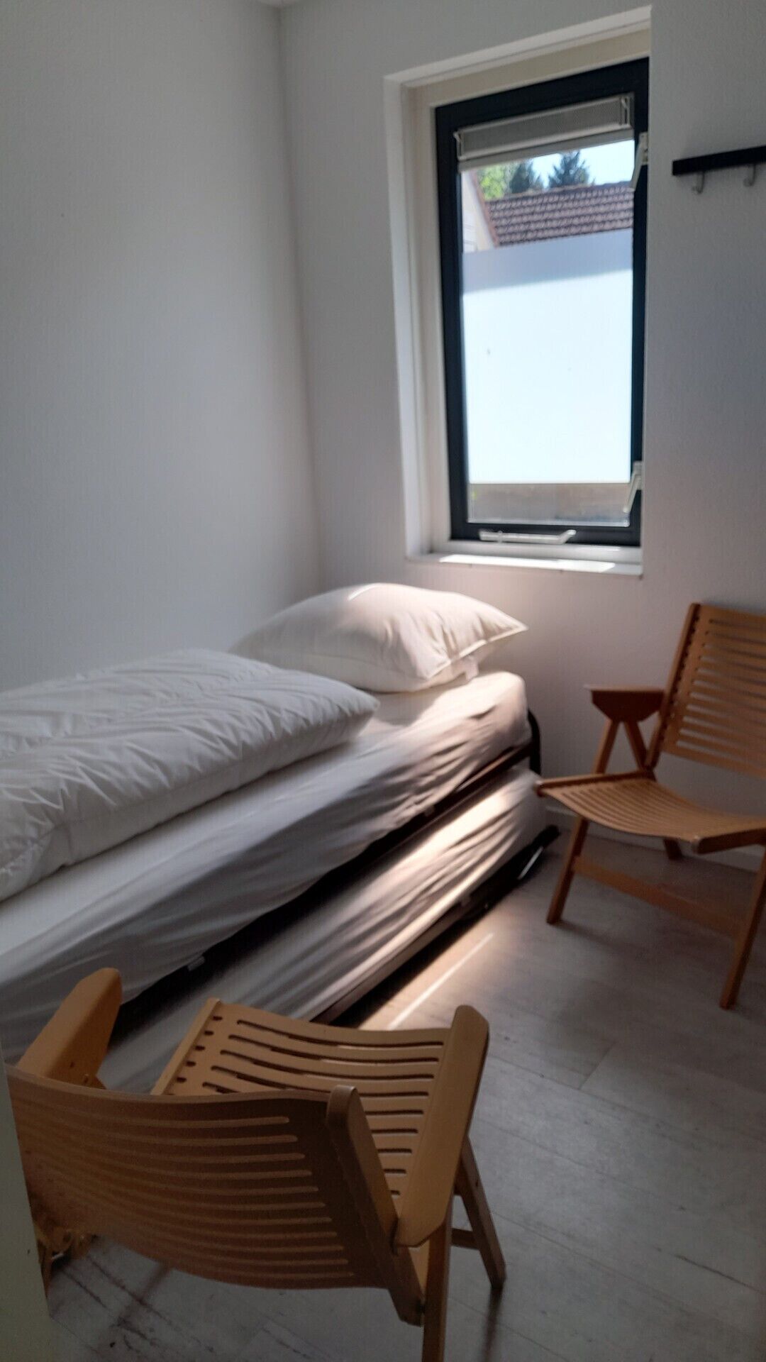 Een slaapkamer met een bed, twee houten stoelen, een raam en een wandplank.