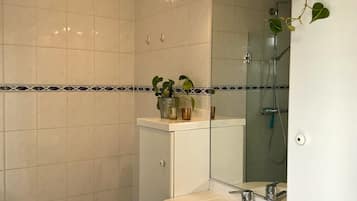 Casa de banho com lavatório branco, espelho e zona de duche.