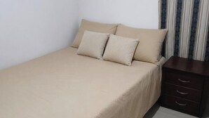 A single bed with a beige bedspread and two pillows, a wooden nightstand with drawers, and a striped curtain. - 3-Bedroom Family Apartment with Pool in Yopal (Villavicencio)