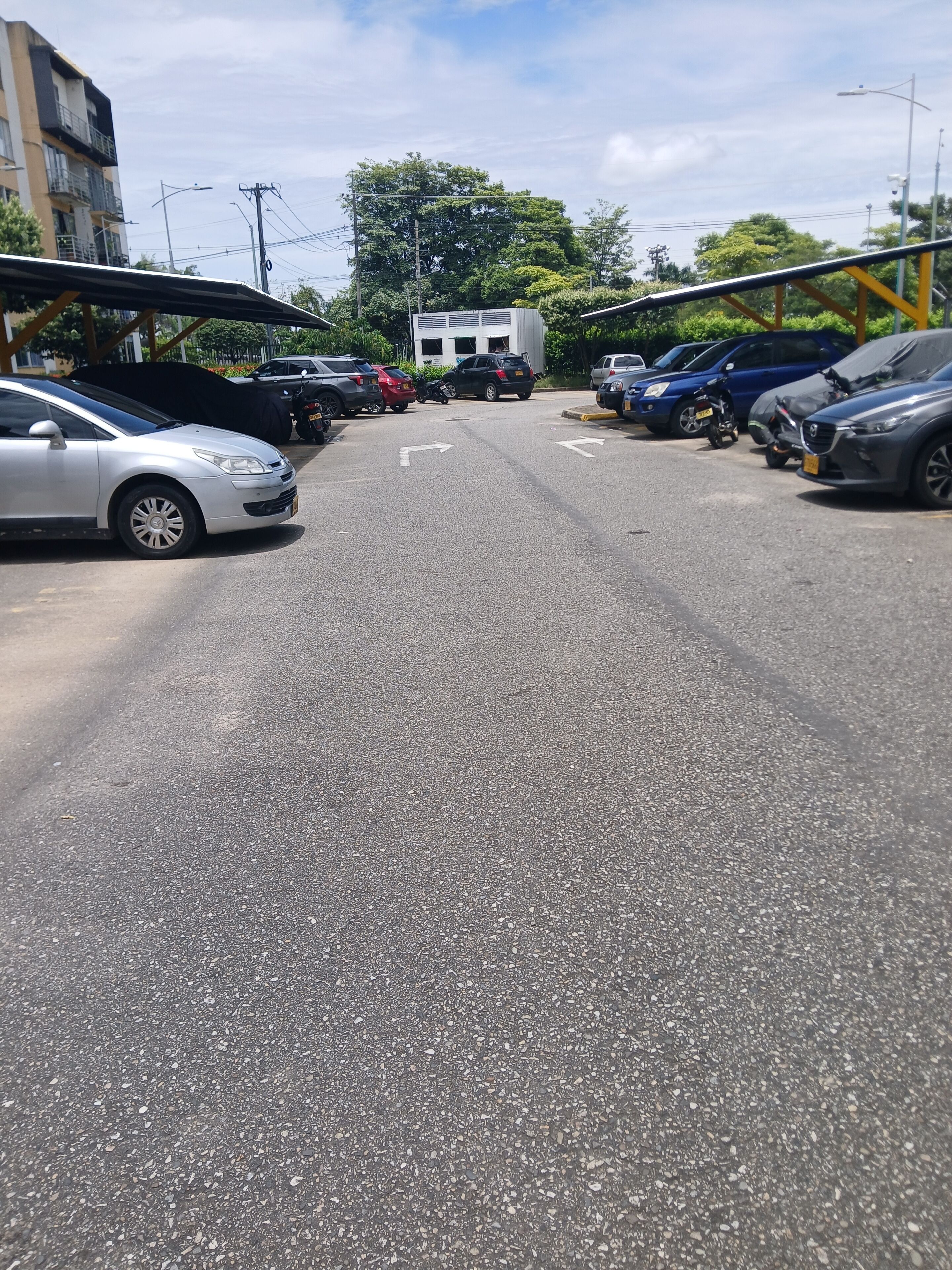 A parking lot with multiple cars and motorcycles, a building in the background, and a clear sky.
