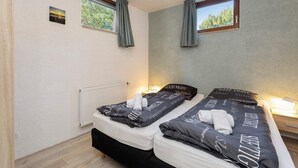 A bedroom with two beds, a window, a radiator, and a small picture on the wall. - Wighenerhorst Bungalow Park - 94 (Wijchen)