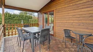 A covered outdoor patio with a table and chairs, wooden walls, and a view of greenery. - Wighenerhorst Bungalow Park - 94 (Wijchen)
