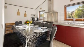 A modern kitchen with a dining area, featuring a large island, red cabinetry, and a view through the window. - Wighenerhorst Bungalow Park - 94 (Wijchen)