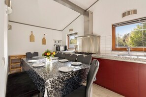 Een moderne keuken met een eethoek, voorzien van een groot schiereiland, rode keukenkastjes en uitzicht door het raam.