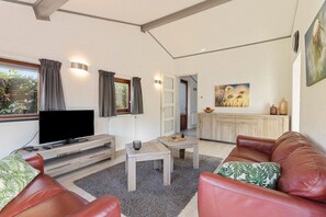 Una sala de estar moderna con televisor, sofás de cuero, una mesa de centro y vistas al exterior.