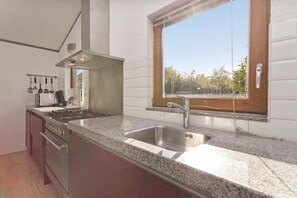 Una cocina con un lavamanos de acero inoxidable, una estufa y un ventanal con vistas a un paisaje natural.