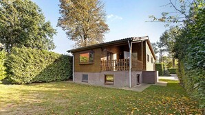 A two-story wooden house with a balcony, surrounded by a well-maintained lawn and hedges. - Wighenerhorst Bungalow Park - 94 (Wijchen)