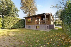Een houten huis met twee verdiepingen en een balkon, omringd door een verzorgd gazon en hagen.