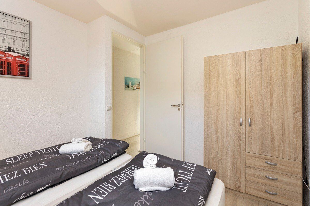 A bedroom with two beds, a wardrobe, and a door leading to another room.