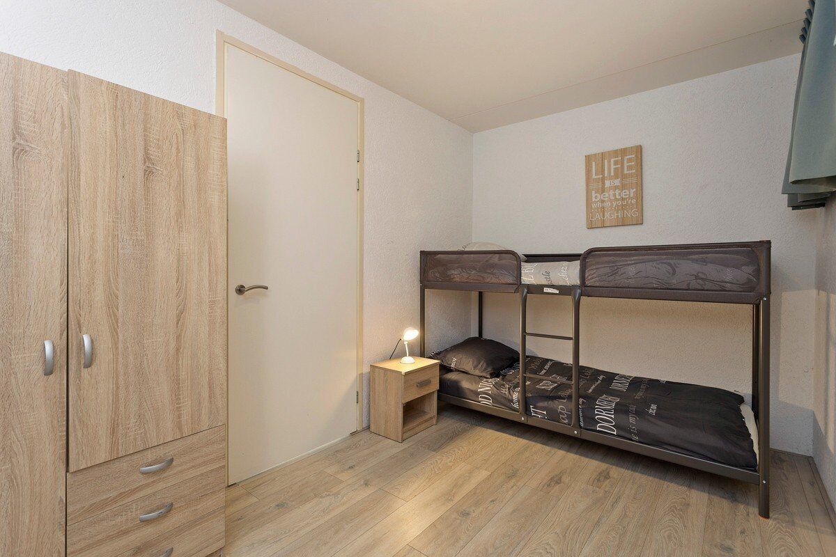 Une chambre avec un lit superposé, une armoire et une table de chevet avec une lampe.