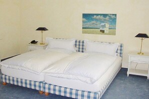 A double bed with a checkered bedspread, two bedside tables with lamps, and a painting of a beach scene on the wall. - in Villa Fortuna by the sea - Apartment 1 (Bansin)