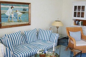 A room with a striped sofa, a glass coffee table with a vase, a wicker chair, a lamp, and a bookshelf. - in Villa Fortuna by the sea - Apartment 1 (Bansin)